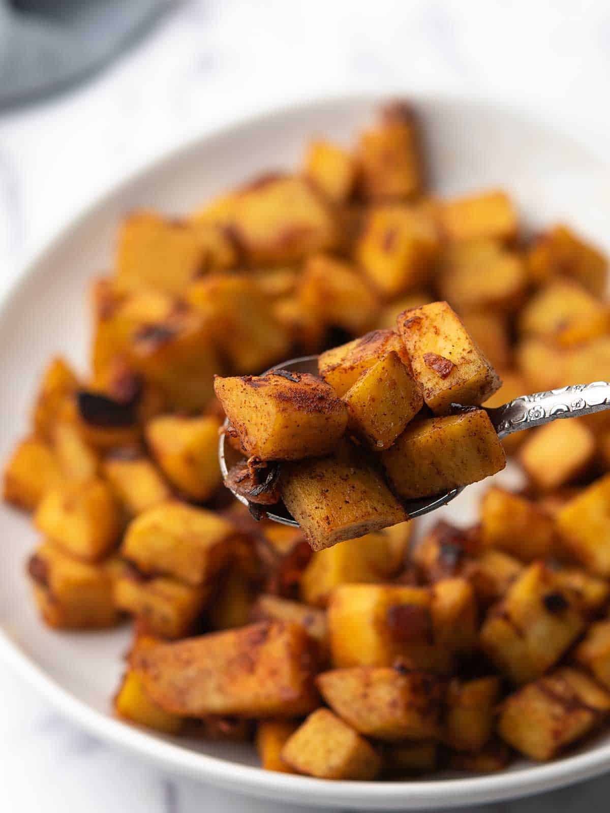 Spoon holding a browned cube of sautéed sweet potato.