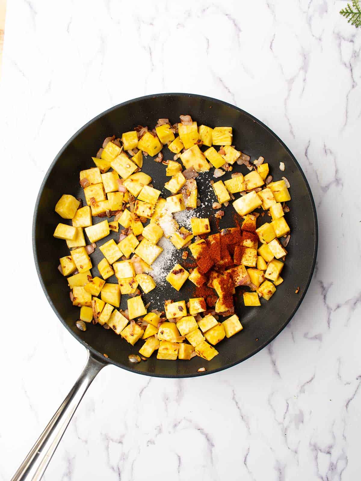 Cubed sweet potatoes coated with smoked paprika and rosemary in a skillet.