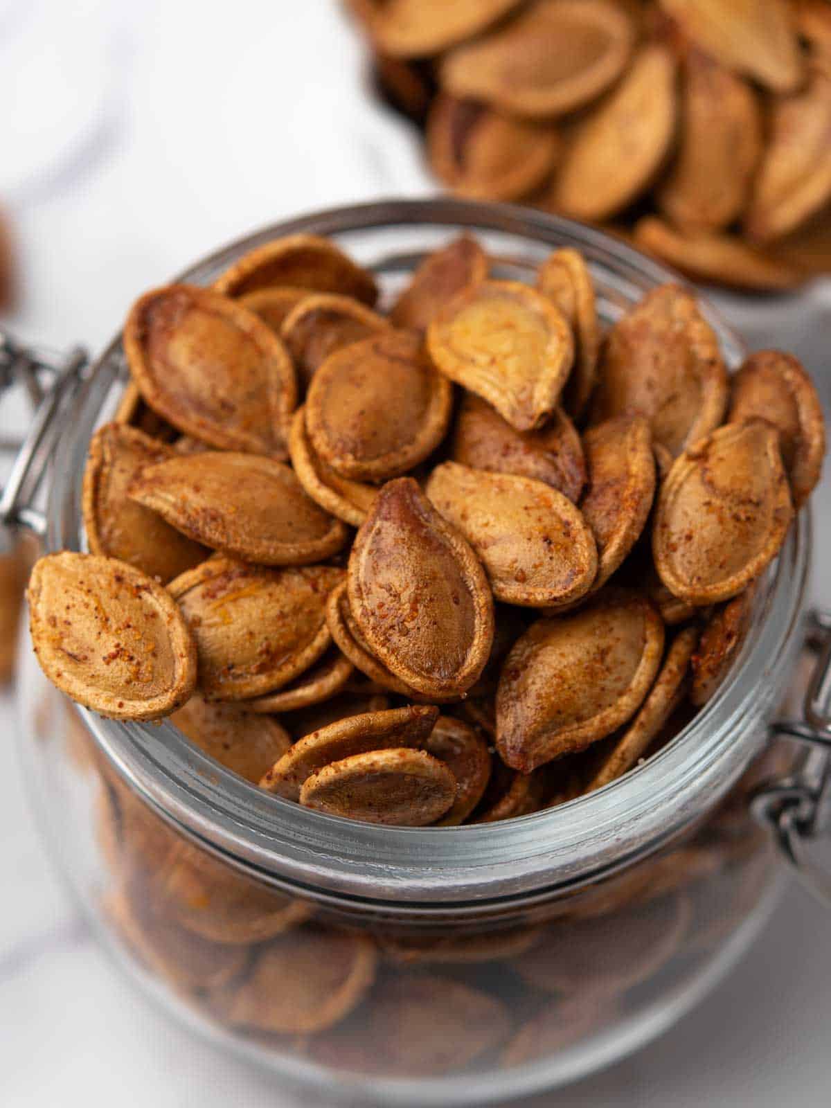 Close-up of seasoned roasted pumpkin seeds in a glass jar, ready for snacking.