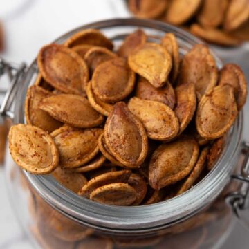 Spicy roasted pumpkin seeds coated with seasoning in a glass storage jar.