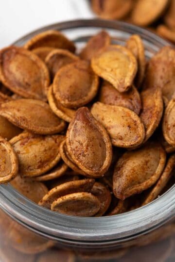 Spicy roasted pumpkin seeds coated with seasoning in a glass storage jar.