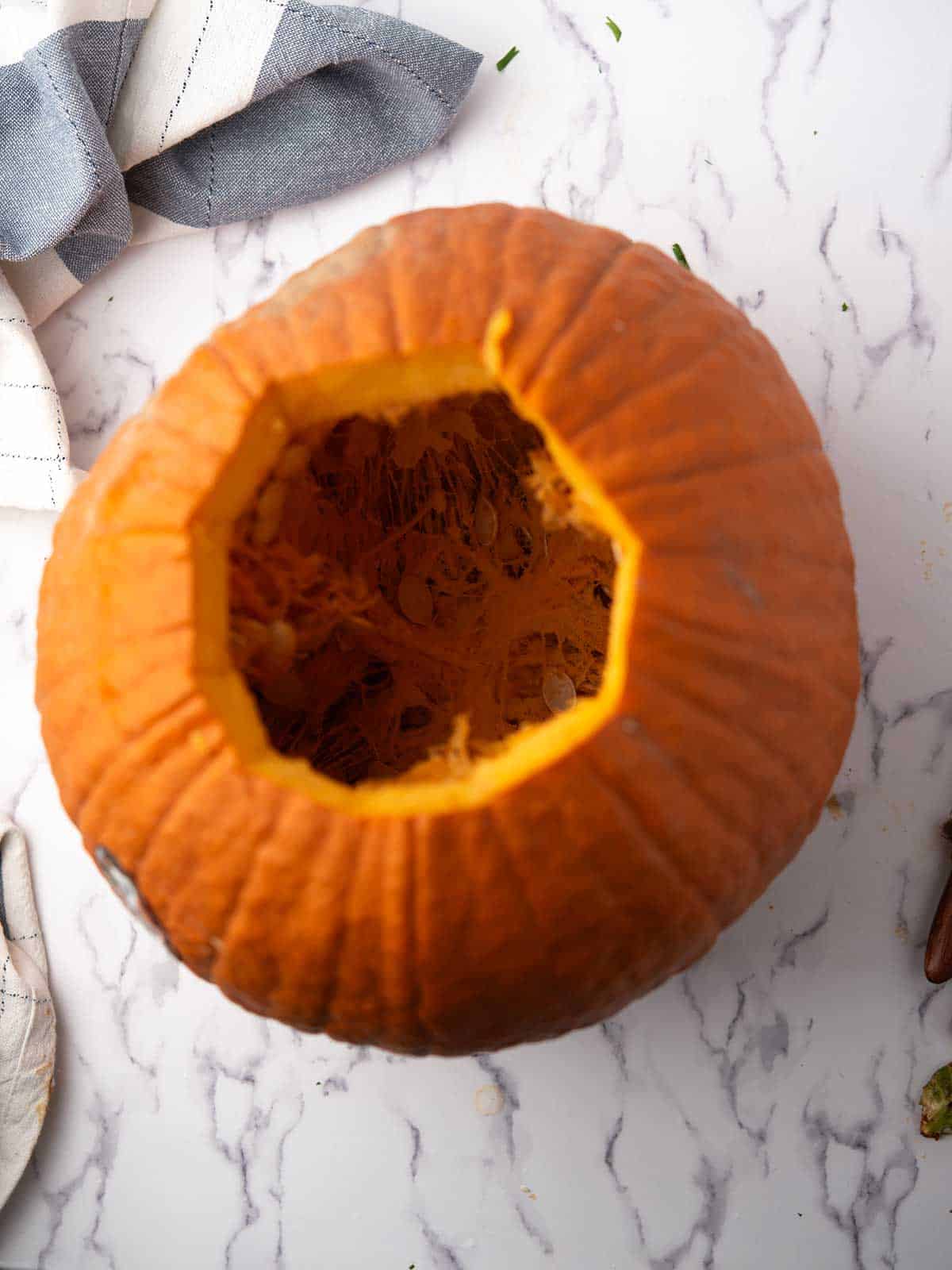 Fresh pumpkin with the top cut open, showing seeds and orange pulp inside.