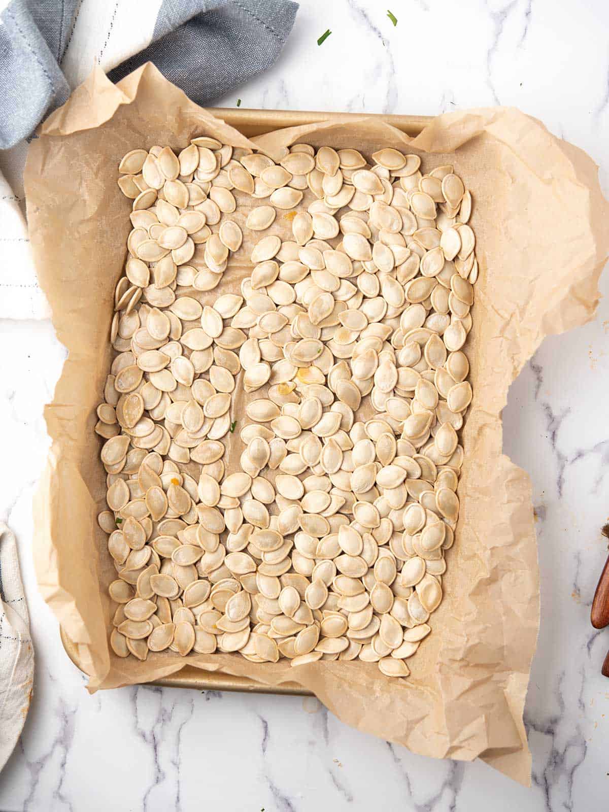 Golden brown roasted pumpkin seeds spread across a parchment-lined baking sheet.