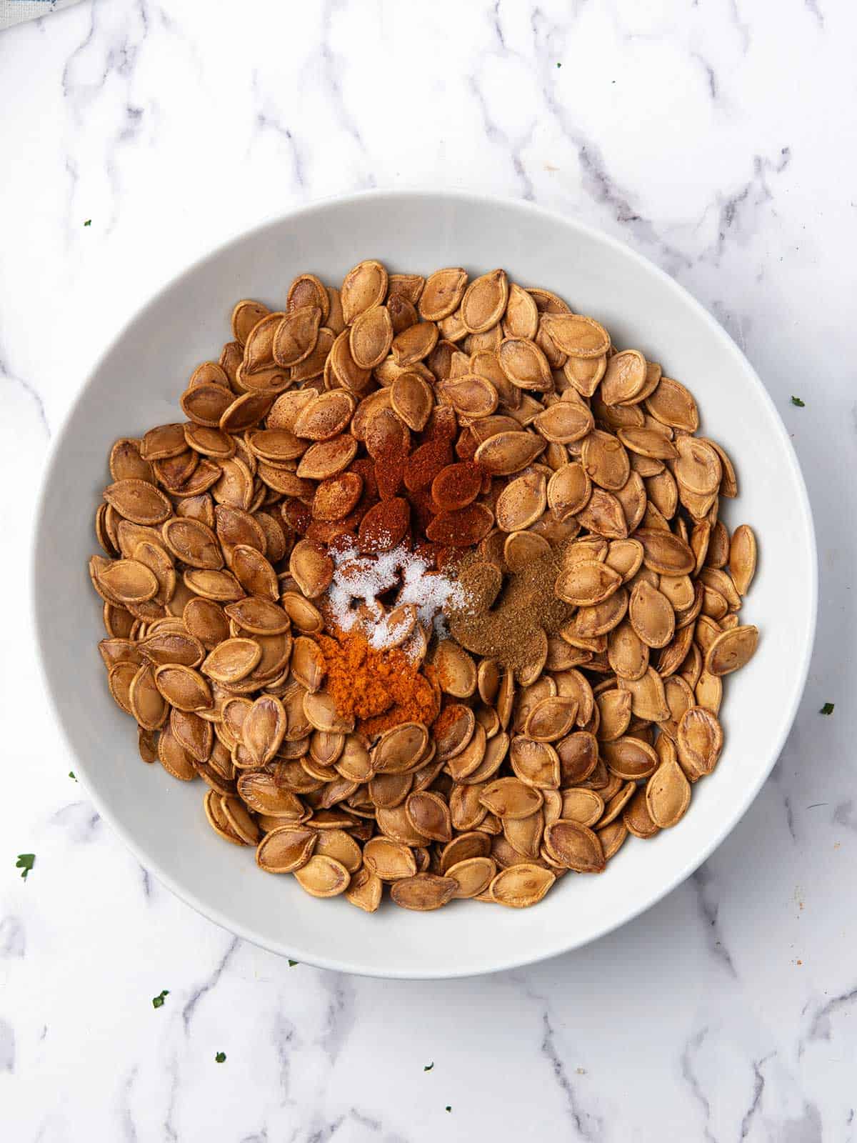 Spicy roasted pumpkin seeds coated with seasoning in a white serving bowl.